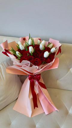 Amour Signature 50 bouquet with red roses and white tulips, wrapped in blush pink paper and finished with a red satin bow.