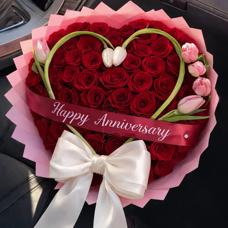 Eternal Love Anniversary Bouquet with red roses, tulip stems forming a heart, pink wrapping, a white bow and a Happy Anniversary ribbon.