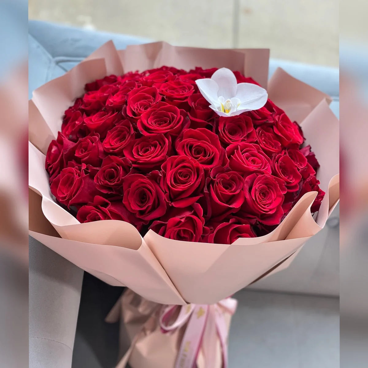 Most Loved Bouquet with red roses and a white orchid accent, wrapped in blush pink paper and tied with a pink ribbon.