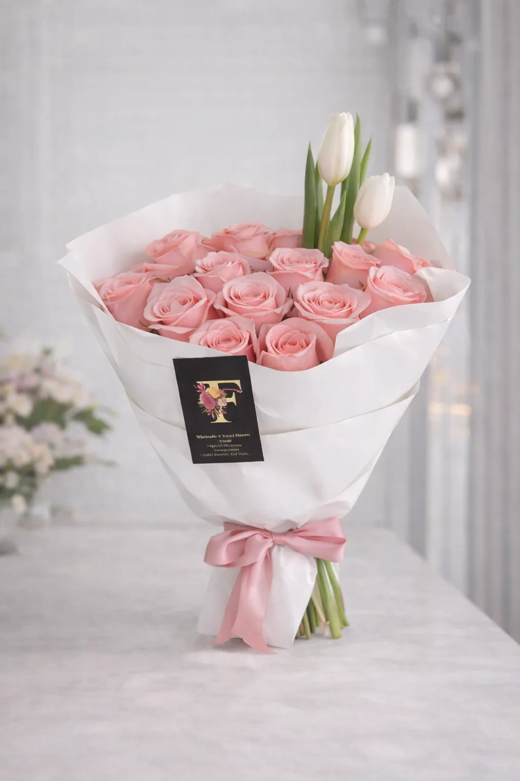 Soft Blush Bouquet with pink roses and two white tulips, wrapped in white paper and tied with a pink satin ribbon.