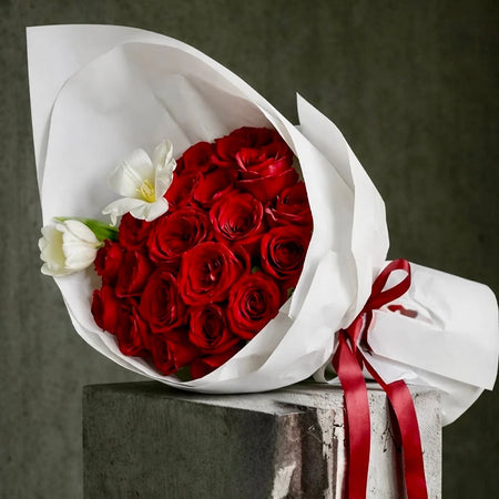 The Velvet 25 bouquet with red roses and white tulips, wrapped in white paper and tied with a red satin ribbon.