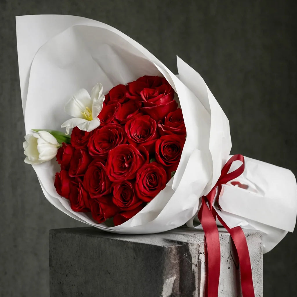 The Velvet 25 bouquet with red roses and white tulips, wrapped in white paper and tied with a red satin ribbon.