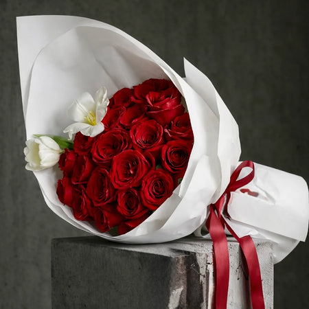 The Velvet 25 bouquet with red roses and white tulips, wrapped in white paper and tied with a red satin ribbon.